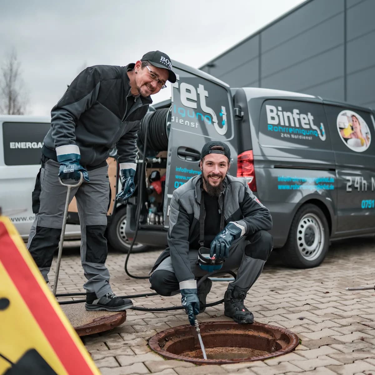 Zwei Mitarbeiter von Binfet Rohrreinigung arbeiten am geöffneten Kanalschacht